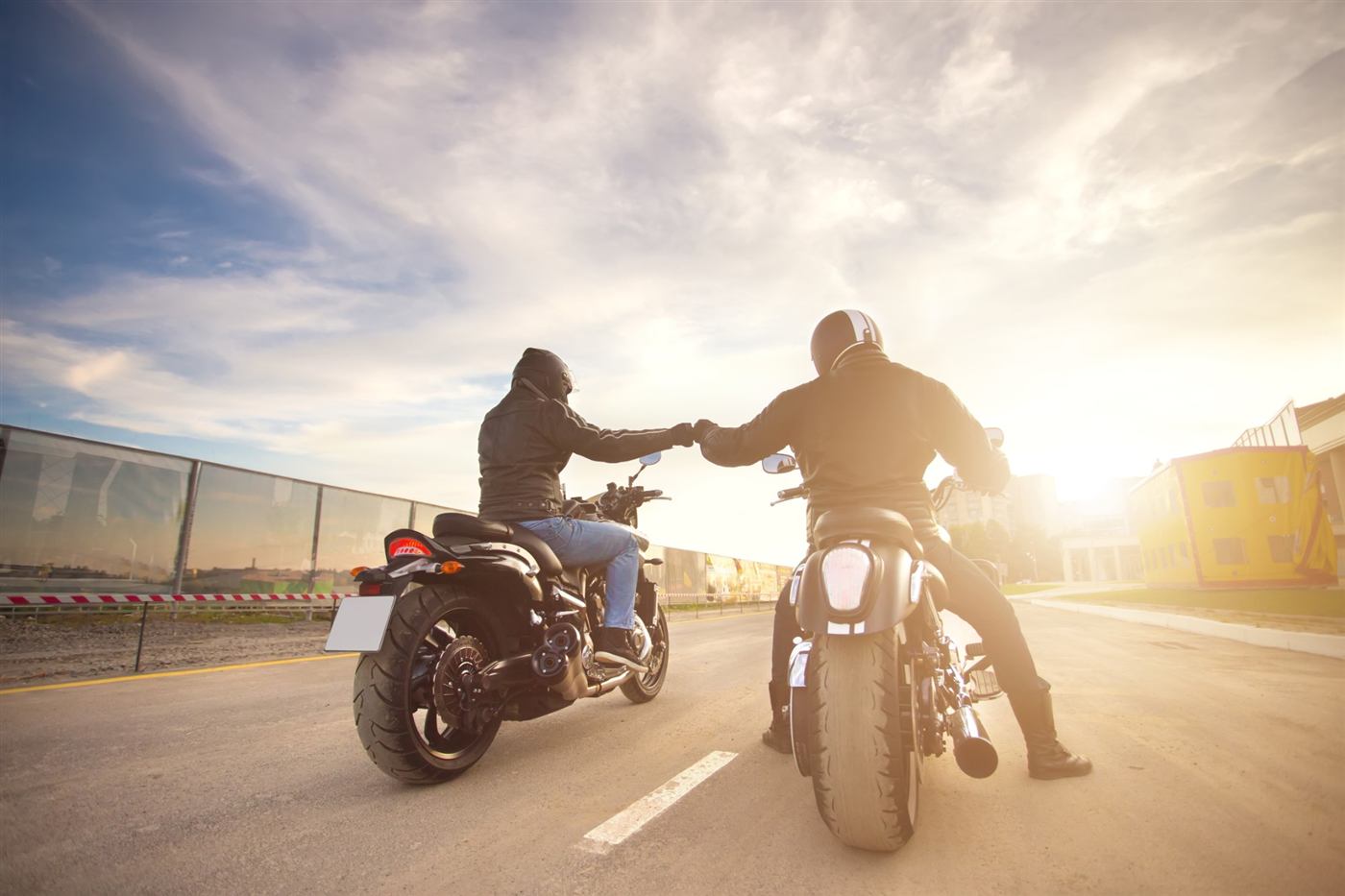 Deux motards se saluent d'un check du poing sur la route au coucher du soleil